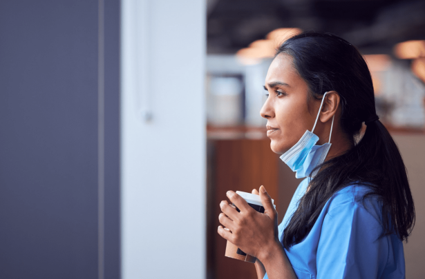 Nurse gazing solemnly out the window while drinking coffee